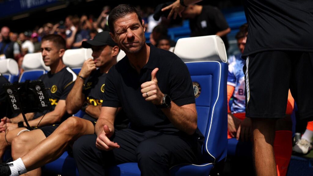 Xabi Alonso seated in the Chelsea dugout giving a thumbs-up.
